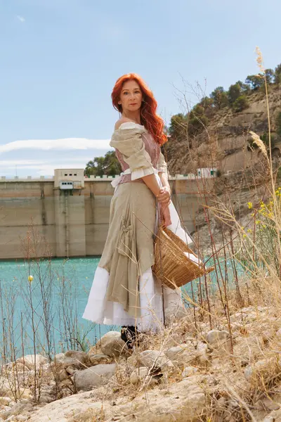 Portrait of a woman dressed as a vintage peasant with the dam of the Amadorio reservoir with low water level due to climate change, Spain
