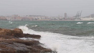 Agua Amarga sahilinde fırtınalı bir deniz manzarası ve arka planda Alicante şehri, İspanya