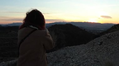 Rüzgarlı bir günde gün batımıyla manzarayı fotoğraflayan kadın, Petrer, İspanya