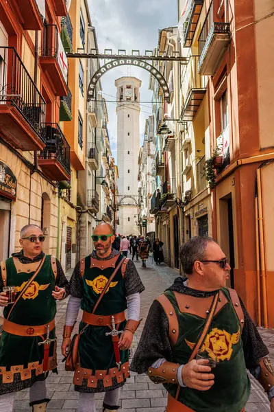 Alcoy, İspanya, 04-05-2025: Koruyucu aziz şenlikleri sırasında arka planda çan kulesiyle San Francisco Caddesi 'nde yürüyen parti katılımcıları.
