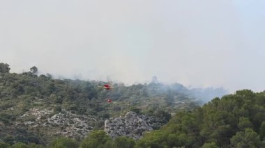 Tanınmayan bir helikopter pilotu Temmuz 2025 'te İspanya' daki Ibi orman yangınını söndürmek için hayatını tehlikeye atıyor..