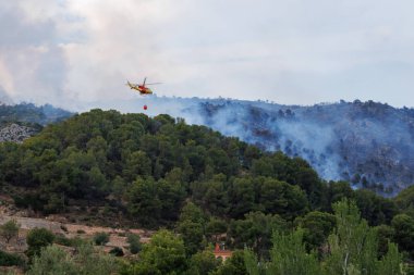 Bambi Bucket ile 112 acil durum helikopteri 18 Temmuz 2025 'te, İspanya' daki Font Roja doğal park yangınında yangına yaklaşıyor.