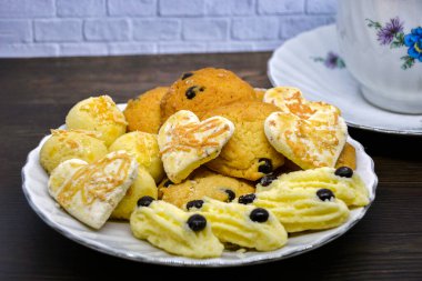 Leziz Endonezya Lebaralı pastaları: Kastengel Pastası, Nastar Pastası, Semprit Pastası ve bir bardak çayla birlikte beyaz bir tabakta duran çikolatalı Kurabiyeler