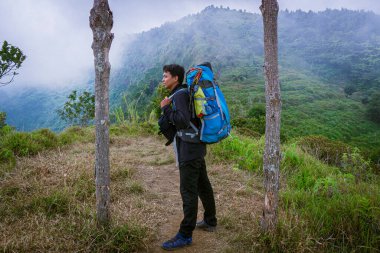 Mavi bir dağcılık çantası taşıyan Asyalı bir dağcı Igirmranak tırmanma rotasındaki Prau Dağı 'ndaki Cendani Tepesi' nde fotoğraf çekiyor.