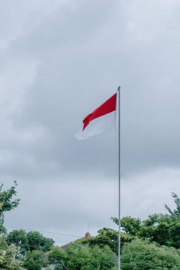 Bu resim Endonezya 'nın görkemli bayrağı Merah Putih' i yakalıyor, en uzun bayrak direğinin üzerinde gururla dalgalanırken, dramatik bir bulutlu arka plan üzerine kurulmuş.