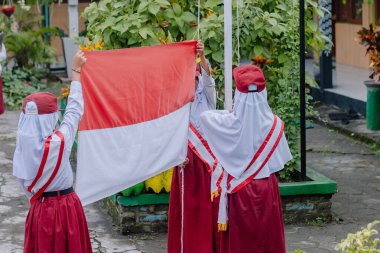 Tören sırasında üç ilkokul çocuğu kırmızı ve beyaz Endonezya bayrağını sallıyor.