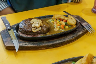 Kalın, sulu bir biftek ve fırında kızartılmış patates. Kırmızı et, altın patates ve yeşil otlar arasındaki zıtlık görsel olarak çekici bir yemek oluşturur..