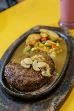 Kalın, sulu bir biftek ve fırında kızartılmış patates. Kırmızı et, altın patates ve yeşil otlar arasındaki zıtlık görsel olarak çekici bir yemek oluşturur..