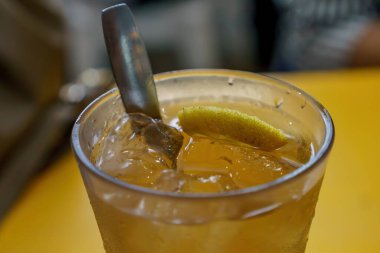 Limon dilimli ferahlatıcı bir bardak buzlu limon çayı, bir tutam nane ile süslenmiş, kaşıkla servis edilmiş.