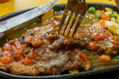 Lezzetli soslu ve otlarla çevrili kağıt gibi ince bir tavuk bifteğini delen bir çatalın yakın çekimi..