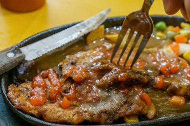 Lezzetli soslu ve otlarla çevrili kağıt gibi ince bir tavuk bifteğini delen bir çatalın yakın çekimi..