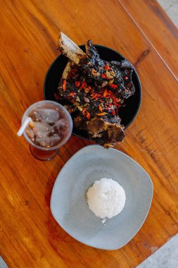 Baharatlı ızgara jumbo kaburga, yanında yumuşak beyaz pirinç ve bir bardak tatlı buzlu çay içeren tam bir yemek..