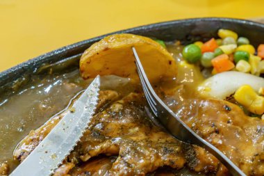 Bir çatal, buruşmuş bir tavuk kağıdının üzerinde patates kızartması tutuyor. Yanında da biftek bıçağı var..