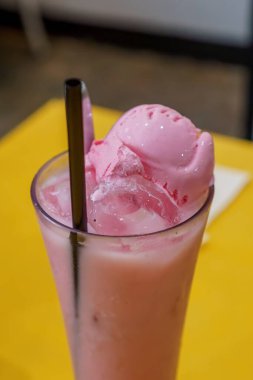 Kalın, kremalı, lezzetli bir çilekli milkshake 'in yakın çekimi. Milkshake krem şanti ve taze çilekle kaplı.
