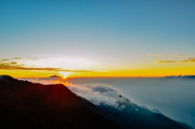 Endonezya 'nın Guntur Dağı' nın tepesinden yayılan ve dağların tepesinden yayılan ışık huzmeleriyle birlikte büyülü bir gün doğumu manzarası.