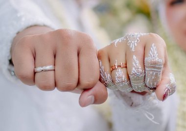 Gelin ve damat, makro fotoğrafçılık teknikleri kullanarak yumruklarını sıkarak alyanslarını gösteriyorlar.