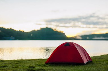 Gölün kenarında kırmızı bir çadır duruyor. Sabah güneşi bulanık gölün kenarında beliriyor.