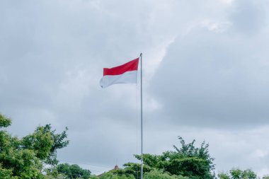 Bu resim Endonezya 'nın görkemli bayrağı Merah Putih' i yakalıyor, en uzun bayrak direğinin üzerinde gururla dalgalanırken, dramatik bir bulutlu arka plan üzerine kurulmuş.