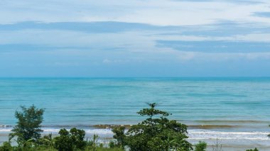 Sahile çarpan mavi gökyüzü, beyaz bulutlar ve dalgalarla dolu güzel bir sahil manzarası. Jodo Plajı, Batang, Endonezya
