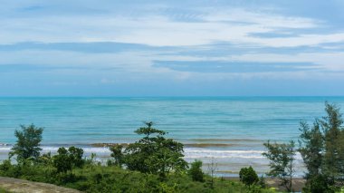 Sahile çarpan mavi gökyüzü, beyaz bulutlar ve dalgalarla dolu güzel bir sahil manzarası. Jodo Plajı, Batang, Endonezya