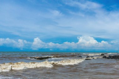 Celong Sahili, Batang, Endonezya 'nın güzel bir hava manzarası. Kahverengi dalgaların mavi gökyüzü ve beyaz bulutlarla kayalara çarptığını gösteriyor.