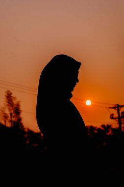 Canlı turuncu bir günbatımına karşı tesetteki bir kadının çarpıcı silueti umudu, maneviyatı ve iç huzuru simgeliyor.