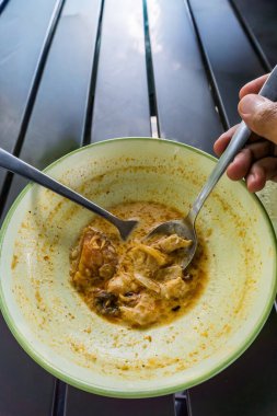 Kaşığı tutan bir el, son kalan lezzetli, zengin Minapadi Tavuk Köri 'sini bir kaseden çıkartıyor.