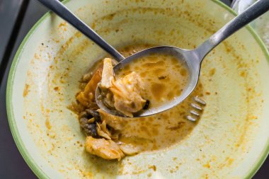 Kaşığı tutan bir el, son kalan lezzetli, zengin Minapadi Tavuk Köri 'sini bir kaseden çıkartıyor.