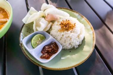 Tüylü pirinç, kızarmış soğan, kraker ve baharatlı sambal ile servis edilen baharatlı Minapadi körili tavuk. Lezzetli ve eksiksiz bir yemek.