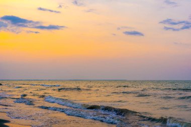 Altın saat sıcak renklerle gökyüzünü boyar, kara bulutlar dalgalı bir denizin üzerinde sürüklenirken. Dalgalar kıyıya vuruyor, bir ışık ve gölge senfonisi.