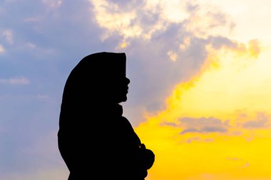 Tegal, Endonezya - 15 Eylül 2024: baş örtüsü içinde Asyalı Müslüman bir kadının silueti çarpıcı bir altın saat günbatımına karşı. Huzurlu ve güzel bir görüntü. Barış ve maneviyat için mükemmel.