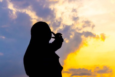 Sarışın Asyalı Müslüman bir kadının silueti büyüleyici bir altın saat günbatımına karşı. Huzurlu ve güzel bir görüntü. Barış ve maneviyat için mükemmel.