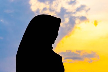 Tegal, Endonezya - 15 Eylül 2024: baş örtüsü içinde Asyalı Müslüman bir kadının silueti çarpıcı bir altın saat günbatımına karşı. Huzurlu ve güzel bir görüntü. Barış ve maneviyat için mükemmel.