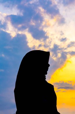 Tegal, Endonezya - 15 Eylül 2024: baş örtüsü içinde Asyalı Müslüman bir kadının silueti çarpıcı bir altın saat günbatımına karşı. Huzurlu ve güzel bir görüntü. Barış ve maneviyat için mükemmel.