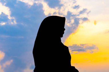 Tegal, Endonezya - 15 Eylül 2024: baş örtüsü içinde Asyalı Müslüman bir kadının silueti çarpıcı bir altın saat günbatımına karşı. Huzurlu ve güzel bir görüntü. Barış ve maneviyat için mükemmel.