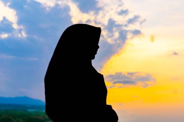 Tegal, Endonezya - 15 Eylül 2024: baş örtüsü içinde Asyalı Müslüman bir kadının silueti çarpıcı bir altın saat günbatımına karşı. Huzurlu ve güzel bir görüntü. Barış ve maneviyat için mükemmel.