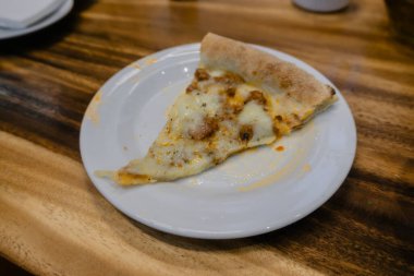 Bu mükemmel dilimlenmiş pizzanın karşı konulmaz cazibesine kapıl. Kırsal bir ahşap masaya karşı beyaz bir tabakta sergileniyor..