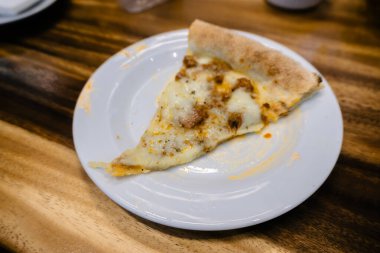 Bu mükemmel dilimlenmiş pizzanın karşı konulmaz cazibesine kapıl. Kırsal bir ahşap masaya karşı beyaz bir tabakta sergileniyor..