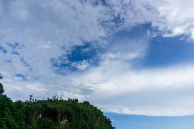 Bu kıyı manzarasının dinginliğini içine çek, canlı, mavi bir gökyüzünün tüylü beyaz bulutlarla kaplı olduğu kıyı şeridi boyunca yemyeşil tepelerle buluştuğu yerde.