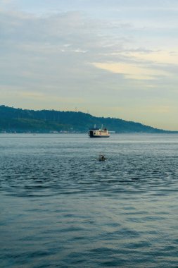 Güneşli bir gökyüzünün altındaki mavi Bali Boğazı 'ndan bir feribot geçiyor.