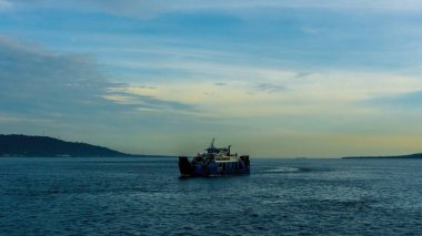 Güneşli bir gökyüzünün altındaki mavi Bali Boğazı 'ndan bir feribot geçiyor.