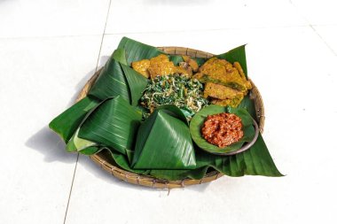 Geleneksel Nasi Pecel yemeği, pilav, sebze ve tempeh, muz yaprakları ve bambu tepsisiyle servis edilir, Endonezya klasiği.