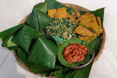 Geleneksel Nasi Pecel yemeği, pilav, sebze ve tempeh, muz yaprakları ve bambu tepsisiyle servis edilir, Endonezya klasiği.