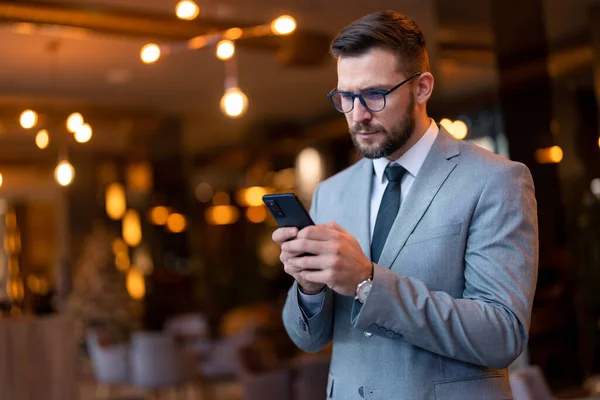 Serious worried businessman receiving unpleasant news on smartphone, reading e-mail or text message. Focused guy in business suit looking at mobile phone screen, scrolling or typing, surfing the internet.