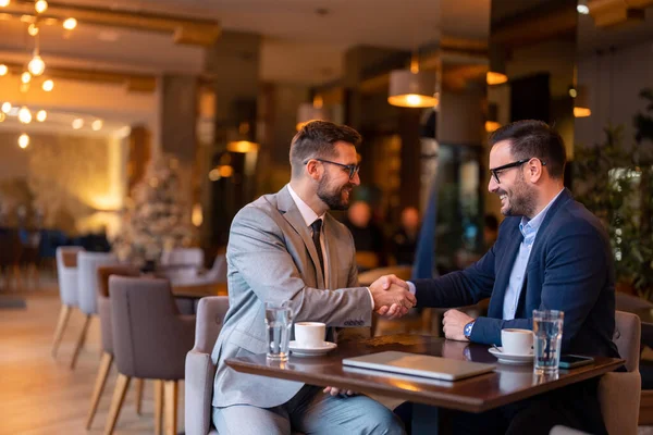 Two men in business clothes, business managers making handshake agreement in restaurant after successful company trade deal. Trade agreement, help and cooperation, partnership handshake concept.