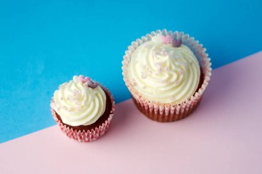 Açık mavi ve soluk pembe arka planda krem peynirli iki kek.