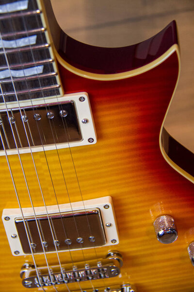 Close up of a solid sunburst from orange to yellow electric guitar with humbucker pickups, without pickguard and gold hardware.