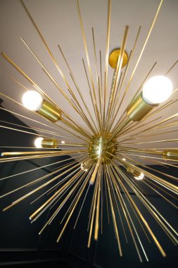 Lüks tasarım lamba, uzamış altın çubuklar ve küre ampulleri ile, sanat deco 70 tarzı, beyaz tavanda ve koyu yeşil duvarda.
