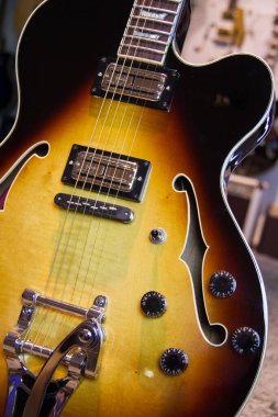 Güneş ışığı altında içi boş bir bedeni siyah-doğal kahverengi ahşap gitarla kaplayın. Humbucker pikaplı, yankesicisiz ve gümüşten donanımsız..