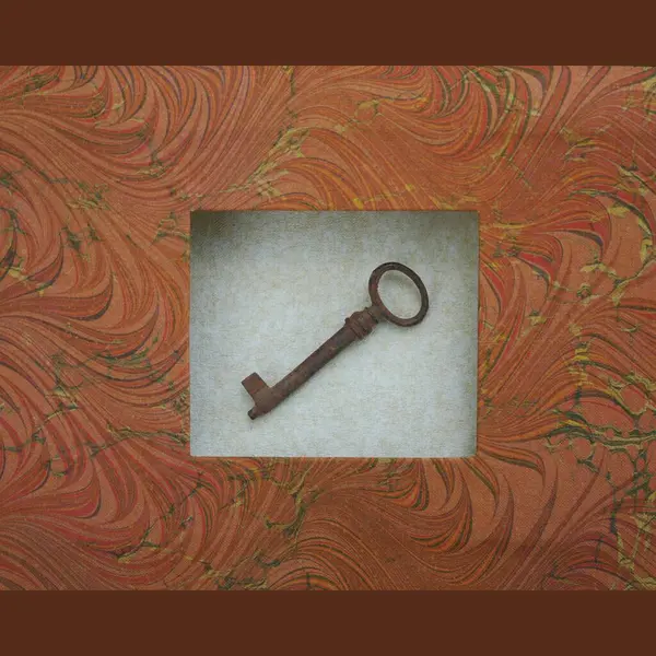 Antique rusty key with round hole placed in a frame on grey background frame of handmade marbled paper, in warm autumn colours, atmospheric minimalist scene, from the front